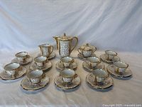 Full lot arranged showing 10 cup and saucer sets, creamer, sugar bowl, and espresso pot on white backdrop.