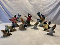 Collection of eleven ceramic Royal Copley bird figurines and vases arranged on a white cloth showing various bird species and colors.