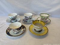 Five vintage floral teacup and saucer sets displayed together showing various floral patterns and gold trimmed rims.