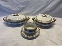 Full view of the oval and round covered serving dishes along with the gravy boat and its underplate showing the matching floral pattern and gold accents on all pieces.