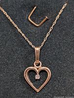 Front view of a 10KT gold heart-shaped pendant necklace with a small diamond in the center of the heart on a 19 inch chain, placed on a dark fabric background.