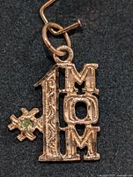 Front view of 10KT gold pendant showing 'MOM' letters, the number '1', and green gemstone detail