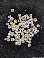 Close up image of assorted loose diamonds varying in size and color on a black background.