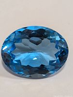 Close-up front view of an oval faceted blue topaz gemstone showcasing its rich blue color and clarity.