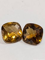 Pair of cushion-cut yellow-orange citrine gemstones, faceted with a checkerboard pattern on the top.