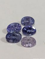 Close-up of five oval tanzanite gemstones showing variation in blue-purple hues and clarity.