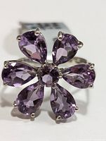Close-up front view of silver flower ring with seven faceted purple amethyst stones arranged as petals and center.