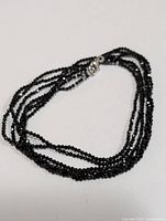 Multiple strands of small faceted black spinel beads forming necklace coiled loosely.