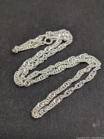 Full view of the silver chain laid out on black background, showing chain length and design.