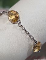 Close-up of two joined oval faceted citrine gemstones bezel set in silver with chain links.