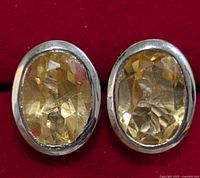 Close-up of front view of two silver earrings each with an oval faceted citrine gemstone in bezel setting