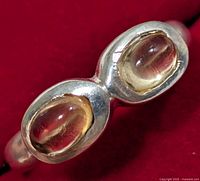 Close-up photo of silver ring with two oval citrine stones on a red background showing the front of the stones.