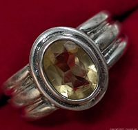 Close-up front view of silver ring set with oval faceted citrine on red background