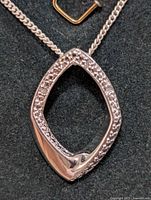 Front view of silver hollow diamond-shaped pendant with small diamonds set around the edges on a silver chain.