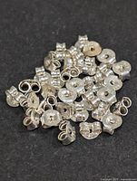 Close-up photo of a pile of various silver earring backs including butterfly and disc styles on a black background.