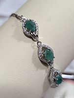 Close-up photograph showing the three emerald stones set in silver with cubic zirconia around each stone on the bracelet.