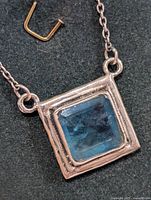 Close-up photo of the square blue gemstone pendant set in a silver bezel with part of the chain visible.