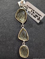 Close-up photo of silver pendant with three linked lemon quartz stones, bezel set, with a visible weight and carat tag