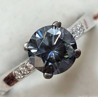 Close-up front view of silver ring with large round moissanite center stone and smaller accent stones on band.