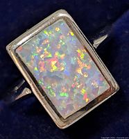 Close-up of silver ring with rectangular opal showing multi-color play of light.