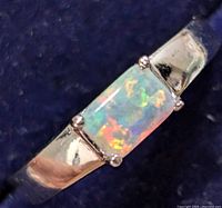 Close-up view of rectangular opal stone with bright multicolor play set in silver band.