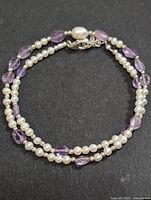 Overall view of double-strand necklace laid flat showing pearl and amethyst beads with silver clasp.
