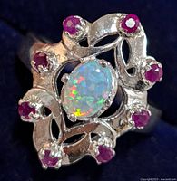 Top view of silver ring showing central oval opal surrounded by eight round rubies on ornate silver setting.