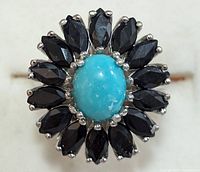 Close-up image of sterling silver ring showcasing turquoise oval center stone and surrounding marquise-cut sapphire stones arranged in floral pattern.