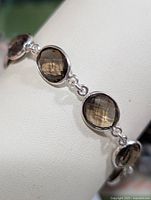 Close-up image showing several bezel set, faceted round smokey quartz stones in a polished silver bracelet link chain.
