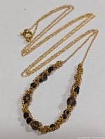 Silver chain necklace laid flat showing faceted smokey quartz beads paired with gold-tone wire mesh elements and a spring ring clasp.