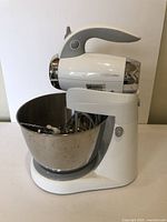 White Betty Crocker stand mixer with stainless steel mixing bowl, showing the whole unit with attachment storage inside the bowl.