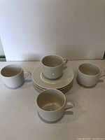 Set of four white coffee cups and five matching white saucers arranged on a table, brand new condition with no chips or cracks.