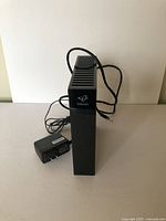 Front and side view of black Hitron modem standing vertically with attached power cord and separate power adapter.