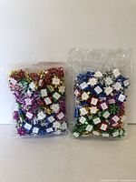 Two sealed plastic bags each filled with hundreds of mini metallic decorative bows in assorted colors including red, green, blue, white, gold, pink, and silver
