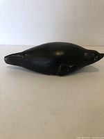 Top view of dark stone Inuit seal carving showing rounded body, snout, and flippers, with visible signature and small repaired area.