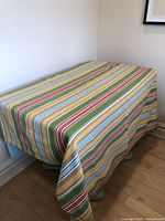 Tablecloth draped over a table showing multicolored stripes horizontally with red, yellow, green, blue, and white. The item is free from visible tears.