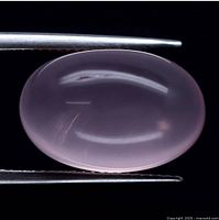 Close-up image of the pink quartz cabochon held by tweezers showing the oval, polished, smooth and glossy surface of the stone.