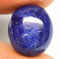 Close-up image of an oval cabochon cut blue sapphire showing deep blue color and internal inclusions.