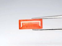 Close-up photo of the rectangular baguette cut orange sapphire gemstone held by tweezers, showing vibrant orange color and clarity.