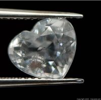 Close-up of heart shaped faceted light pink morganite gemstone held in tweezers showing the cut, clarity, and visible internal inclusions.