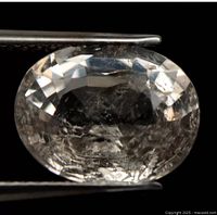 Close-up of oval cut light pink Morganite held by tweezers showing internal inclusions.