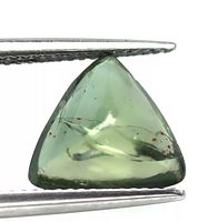 Close-up image showing the triangular cabochon cut of the green apatite, held between tweezers. The stone shows internal inclusions and a translucent green color.