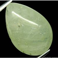 Pear-shaped cabochon cut sapphire with very light green color, held by tweezers showing the smooth polished surface and internal inclusions under lighting.