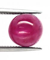 Close-up of round cabochon ruby held by tweezers showing surface texture, color, and inclusions.