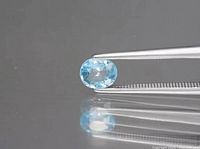 Close-up of oval blue zircon gemstone held by tweezers showing color, cut, and clarity.