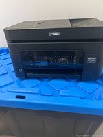 Front and top view of Epson WorkForce WF-2630 printer on a blue surface, showing brand and multi-function panel.