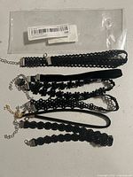 Top view of 6 black chokers laid flat showing different textures and styles including velvet, lace, floral, and braided designs with metal clasps.