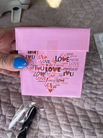 Pink square box with heart design made of 'love' words in various languages and fonts.