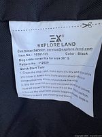 Close-up of label on dog crate cover showing brand Explore Land, item number 10501105, color black, pattern number 312020, and care instructions.