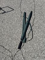 Golf umbrella folded on rough asphalt ground showing overall length and handle.